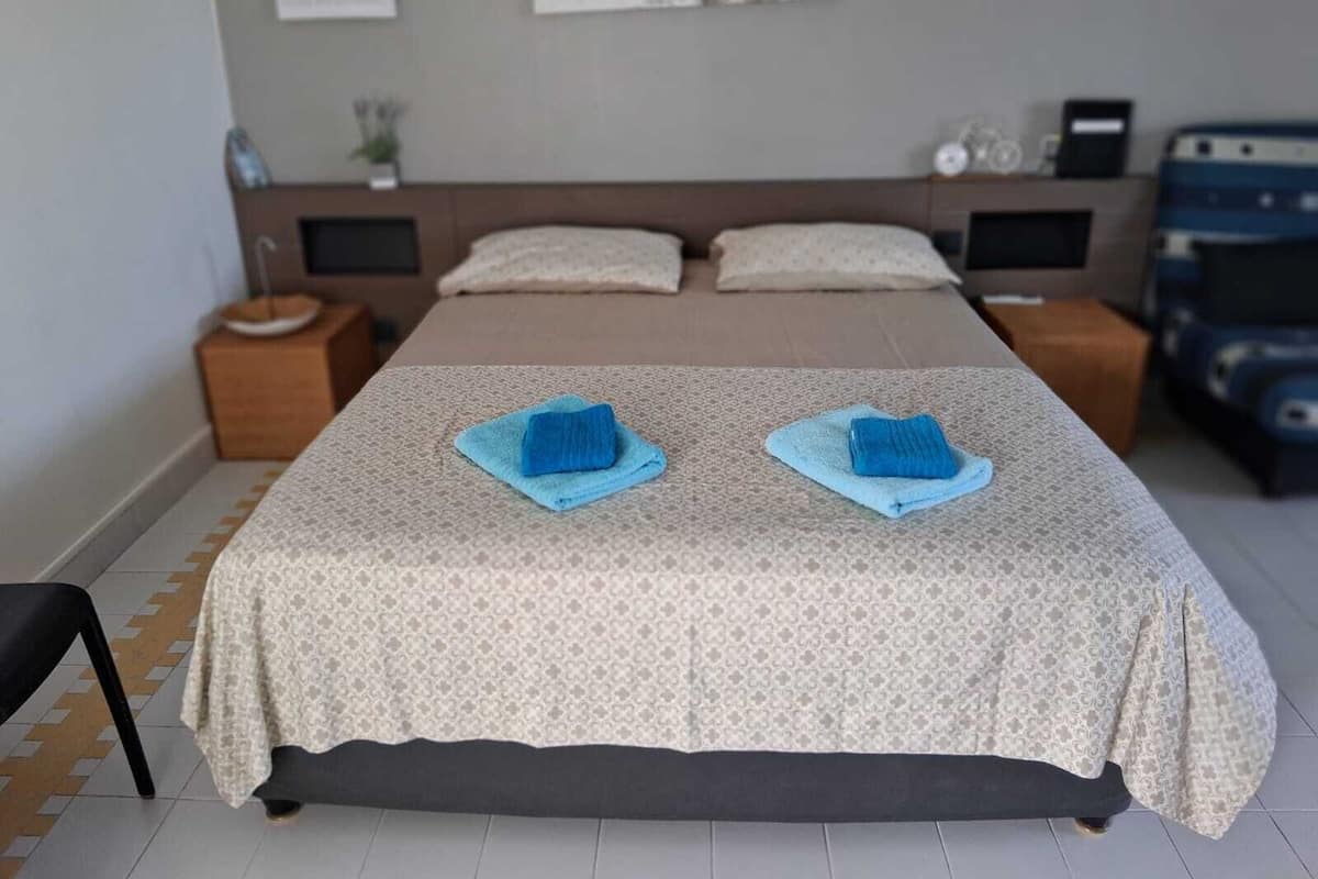 Un lit bien fait, avec deux serviettes bleues, une tête de lit, des tables de chevet et une horloge fixée au mur.