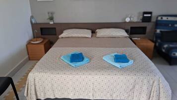 A neatly made bed with two blue towels, a headboard, bedside tables, and a wall-mounted clock.