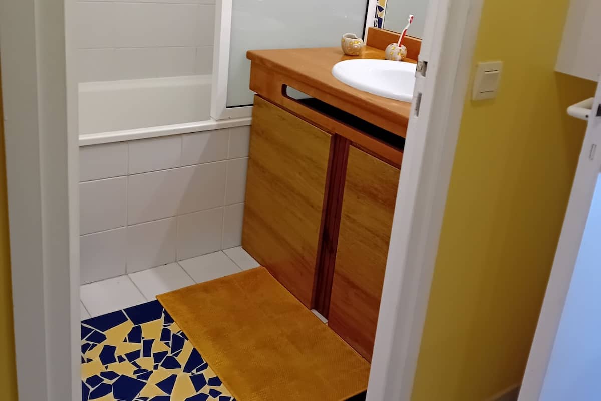 Une salle de bain avec une baignoire blanche, un meuble-lavabo en bois avec un évier, un miroir et un tapis à motifs sur le sol.