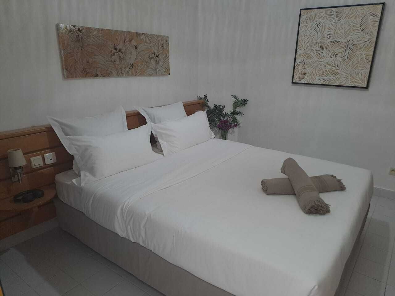 Un letto rifatto con lenzuola bianche, una testiera in legno e un cuscino decorativo.