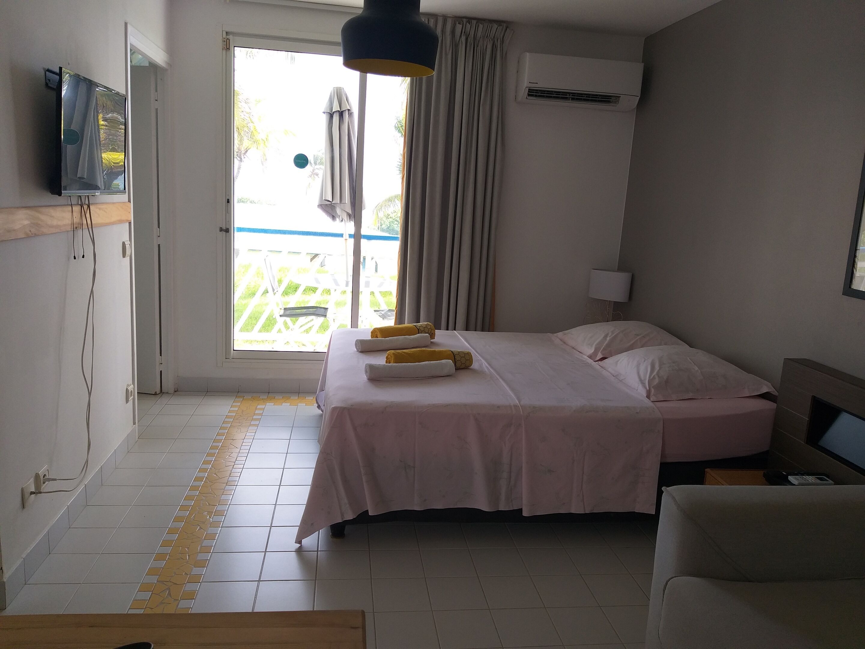 A hotel room with a bed, a sofa, a TV, an air conditioner, and a view of the outside.