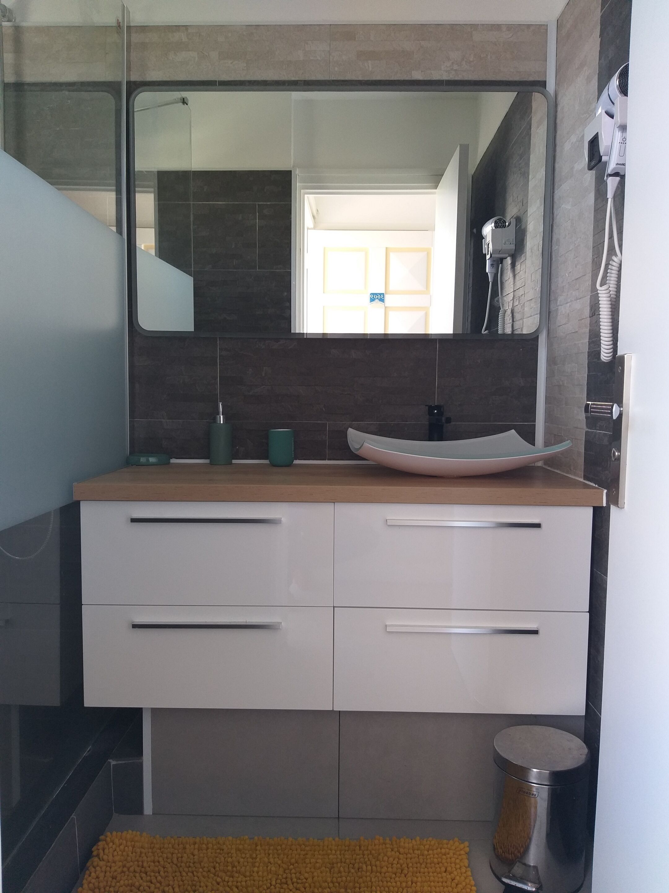Un baño moderno con un espejo grande, un lavabo y un secador de pelo fijado en la pared.