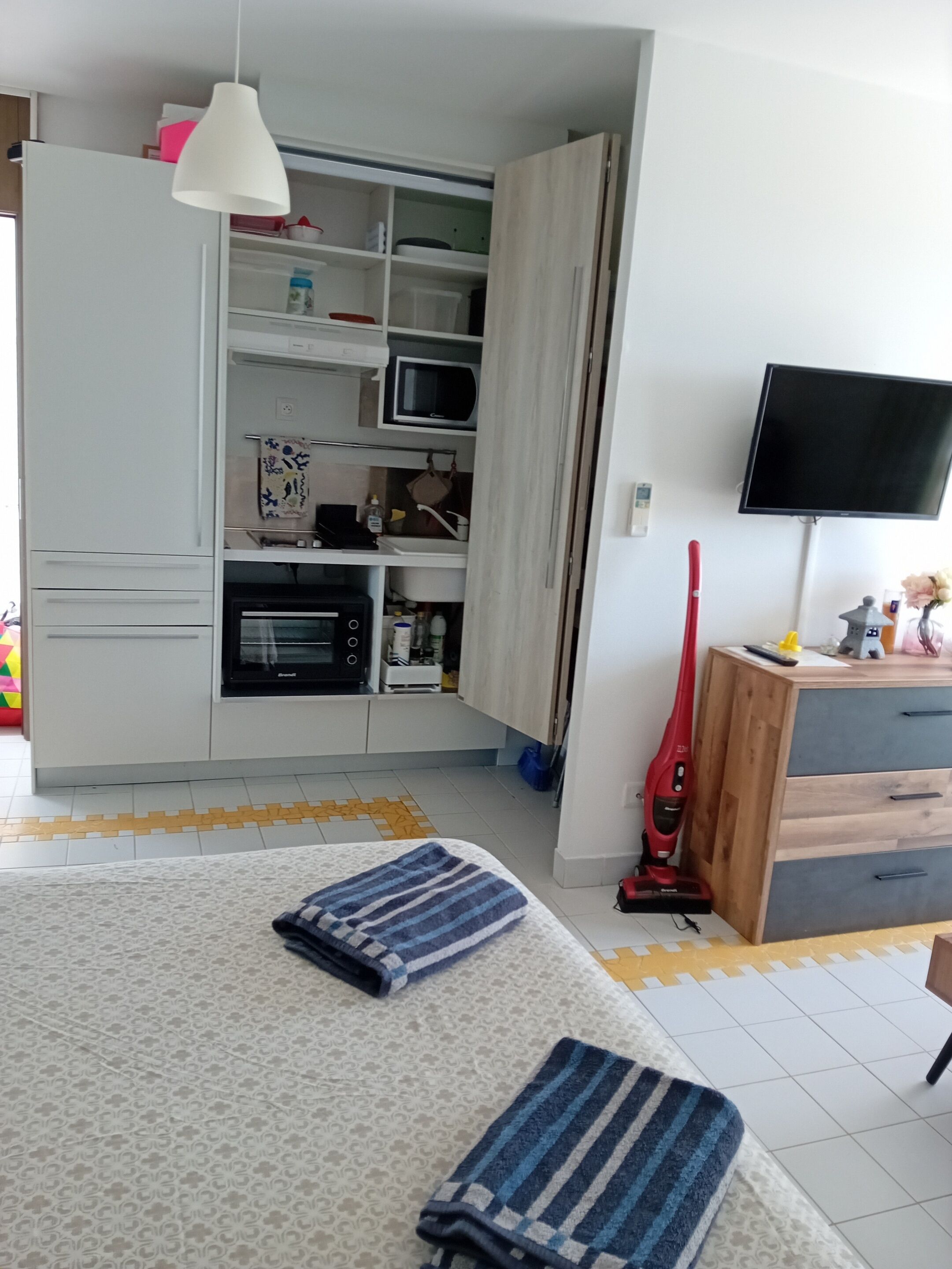 Ein kompakter Wohnbereich mit Küchenzeile, Fernseher und Staubsauger.