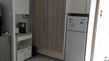 A compact kitchen with a refrigerator, a coffee maker, and a cabinet.