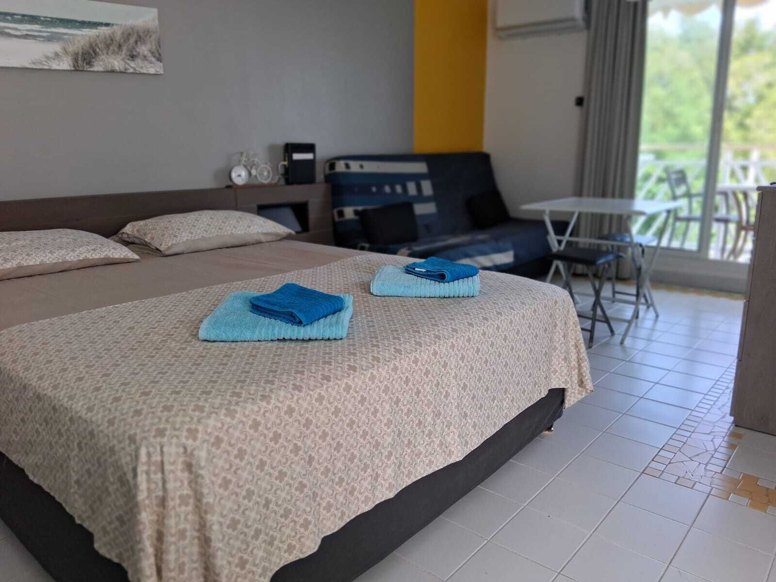 Habitación de hotel con una cama grande, dos toallas azules, una mesita y vistas al exterior.