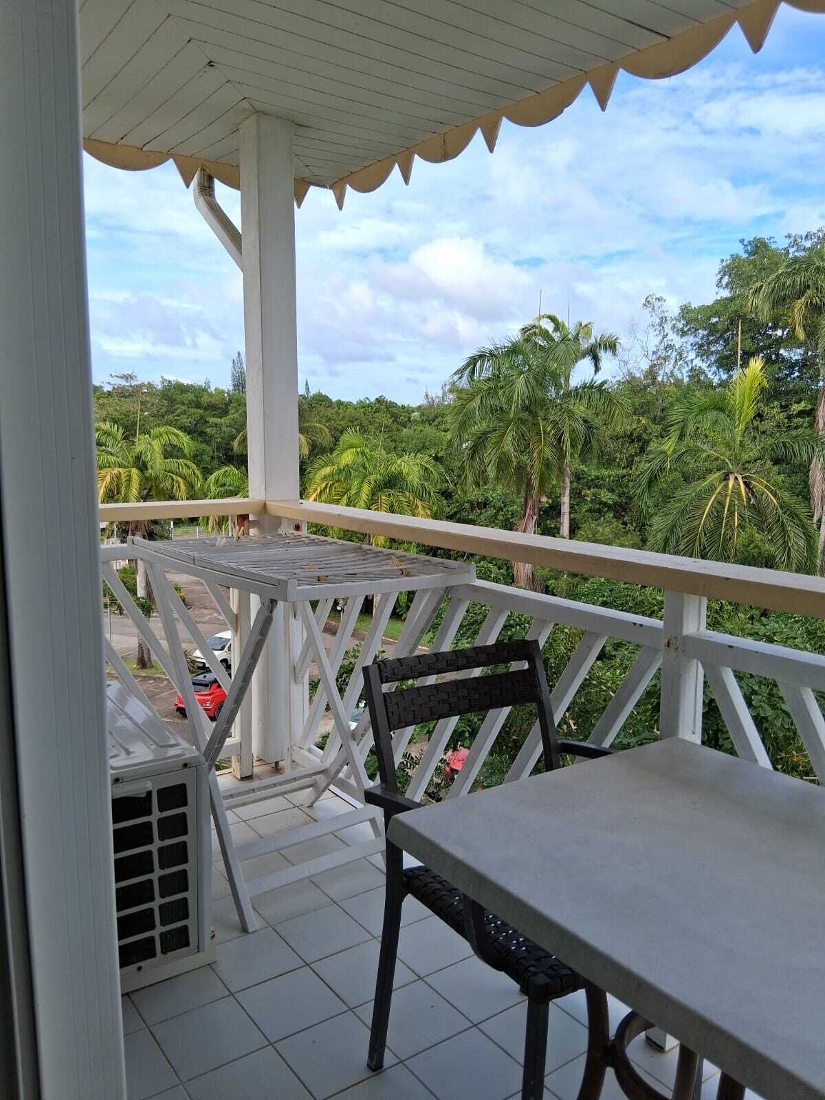 A balcony with a table and chairs, overlooking a lush green landscape with palm trees.