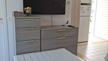 A modern kitchen with a flat-screen TV, grey cabinets, and a white table with a metal frame.