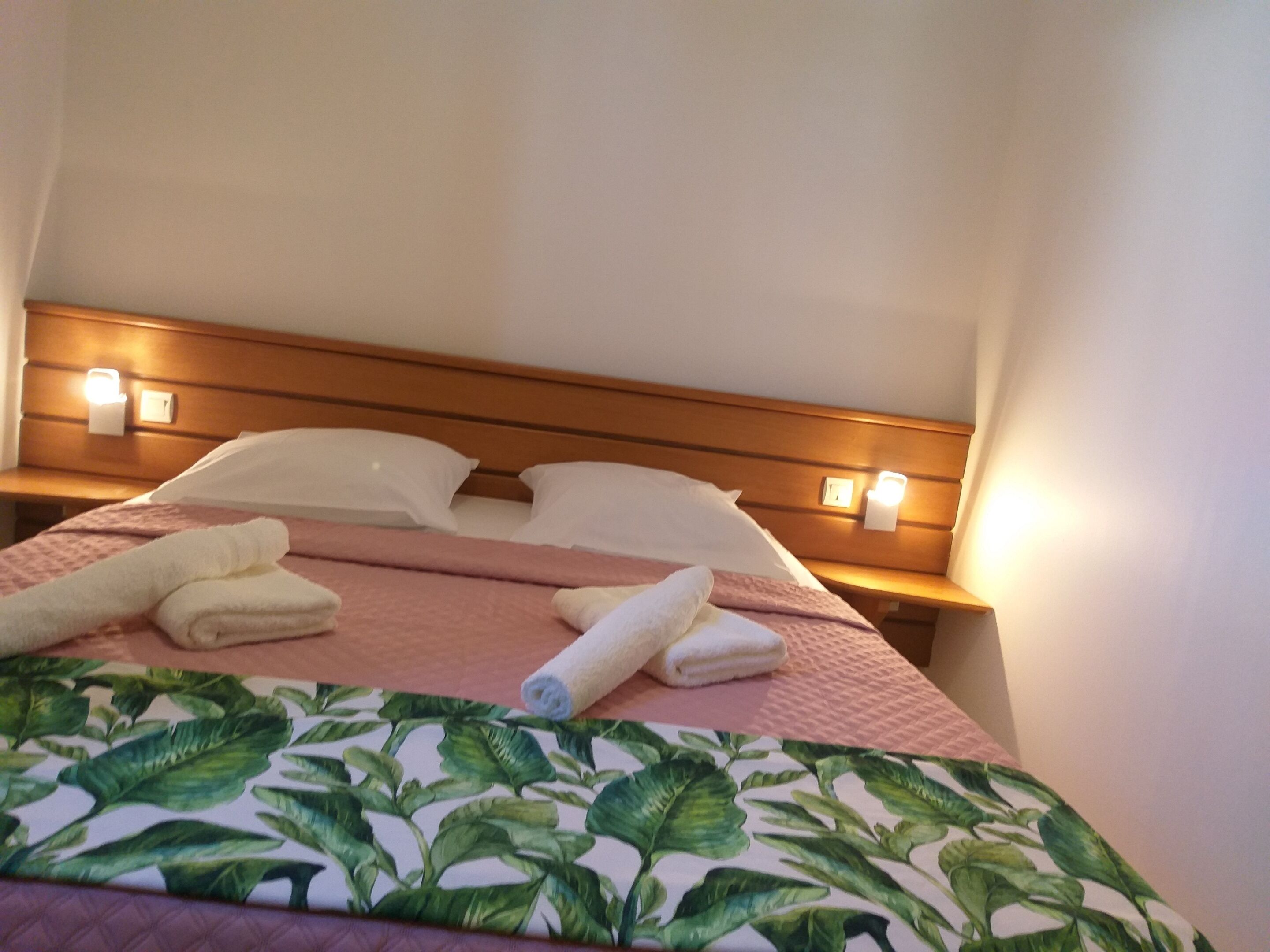 A hotel room with a bed, pillows, a headboard, and bedside lamps.