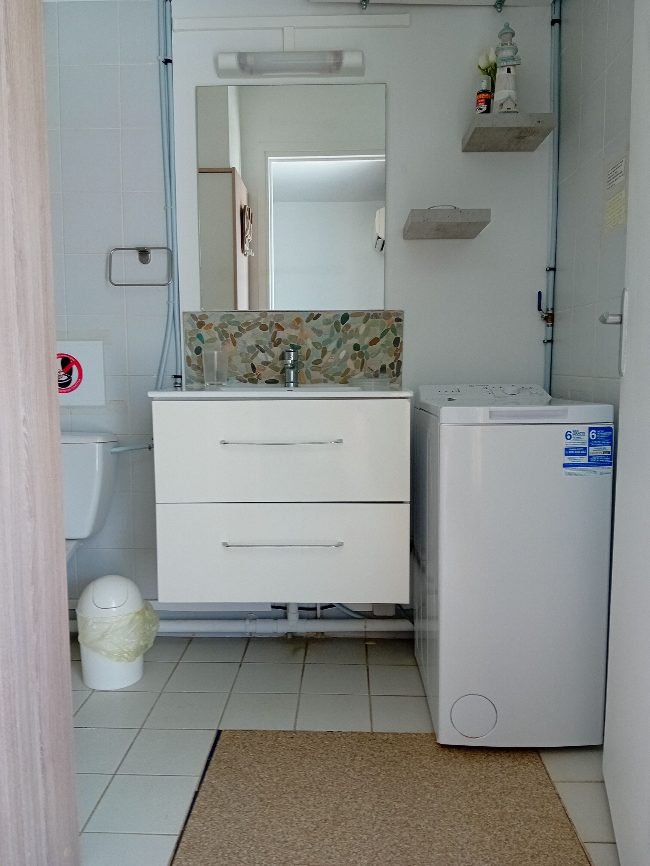 Een compacte badkamer met een witte wastafel, spiegel en een kleine koelkast.