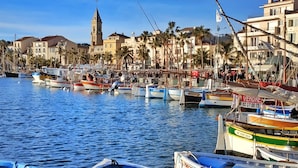 A marina with boats docked, a prominent church tower, and residential buildings along the waterfront. - Large terrace, 50m from beach with sea view + private pool (Six-Fours-les-Plages)