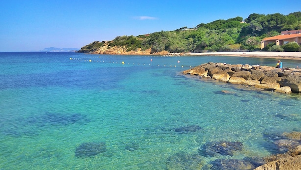 A coastal area with clear turquoise waters, rocky shoreline, and a building with a red roof on a hillside. - Large terrace, 50m from beach with sea view + private pool (Six-Fours-les-Plages)