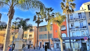 A street with palm trees, a statue, and buildings with balconies. - Large terrace, 50m from beach with sea view + private pool (Six-Fours-les-Plages)