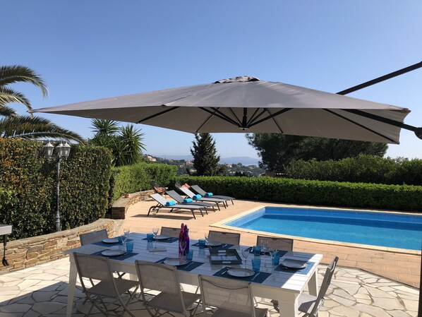 A poolside dining area with a table set for four, a large umbrella, and lounge chairs. - Splendid Sea View Villa near St-Tropez - Pool, AC, Sleeps 10 (Cavalaire-sur-Mer)