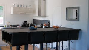 Cocina moderna con una isla central, taburetes de bar y un amplio ventanal.