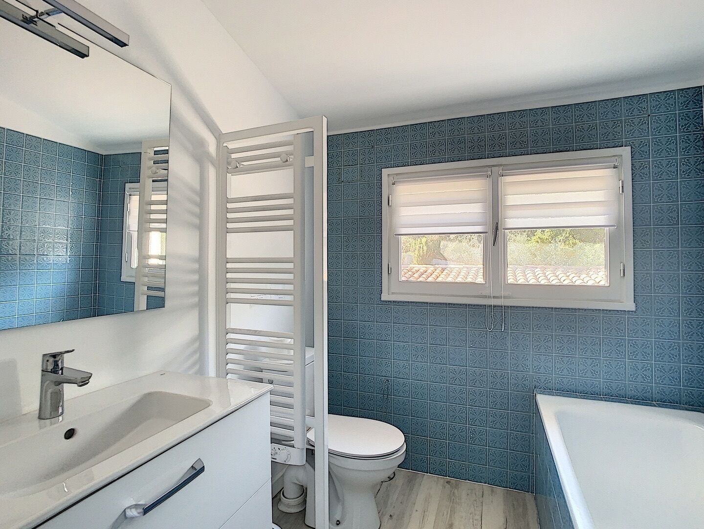 A bathroom with a white sink, toilet, and bathtub. There is a window with blinds and a towel rack.