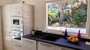 Una cocina moderna con horno empotrado, microondas y un ventanal que ofrece vistas a árboles y follaje exterior.