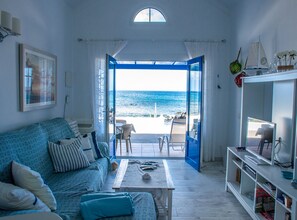 A room with a view of the sea, a sofa, a table, and a bookshelf.