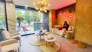 Relax in a cozy seating area with a sofa and armchairs, surrounded by a large window and a unique neon sign.