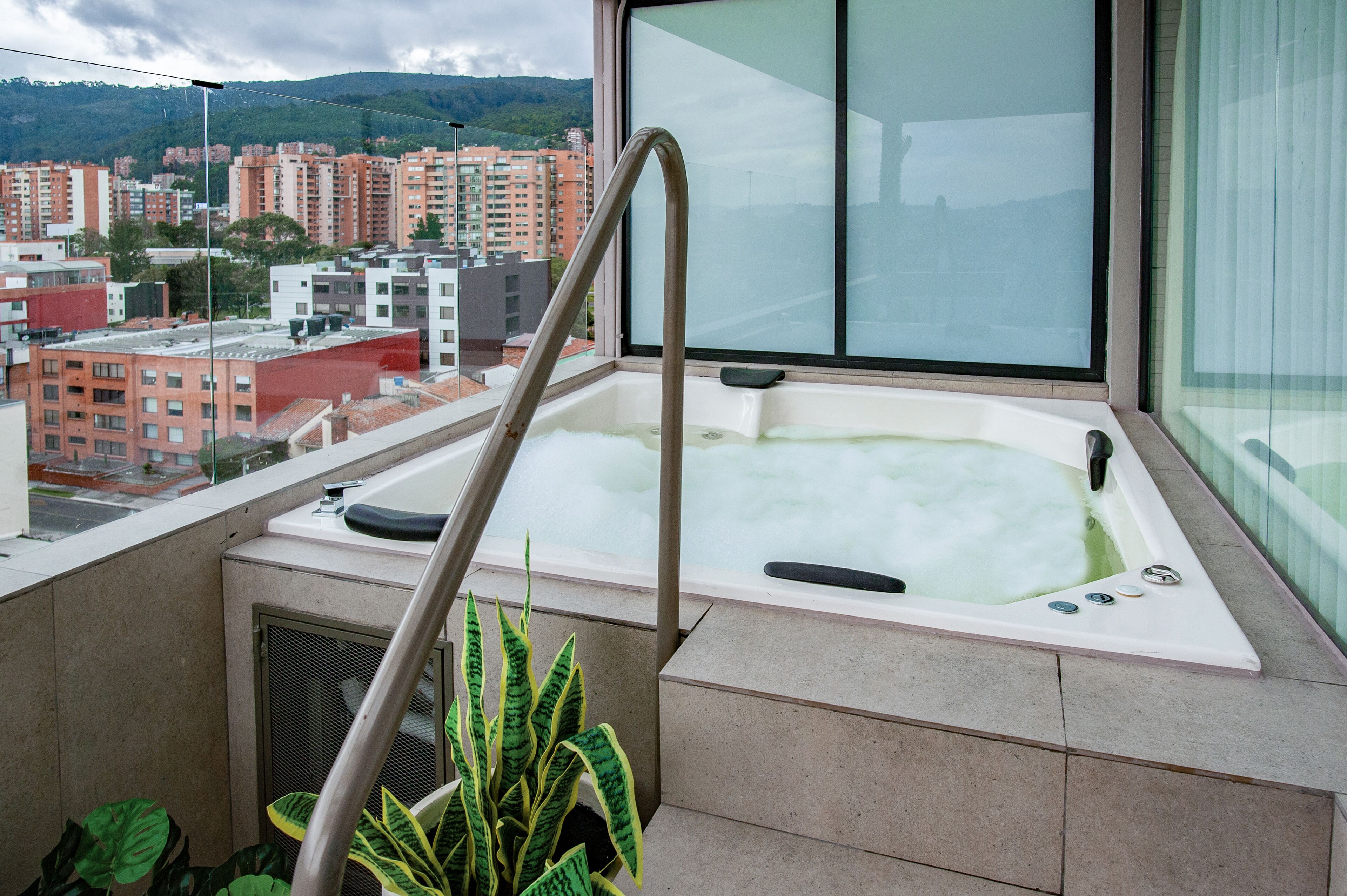 A hot tub with a metal ladder, a view of a cityscape, and a potted plant.
