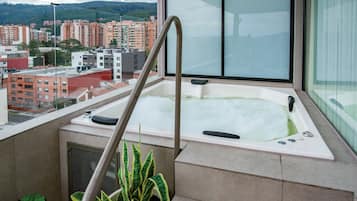 A hot tub with a metal ladder, a view of a cityscape, and a potted plant.
