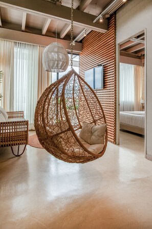 Ein modernes Interieur mit einem hängenden Rattan-Sessel, einem Bett und einem großen Fenster mit Vorhängen.