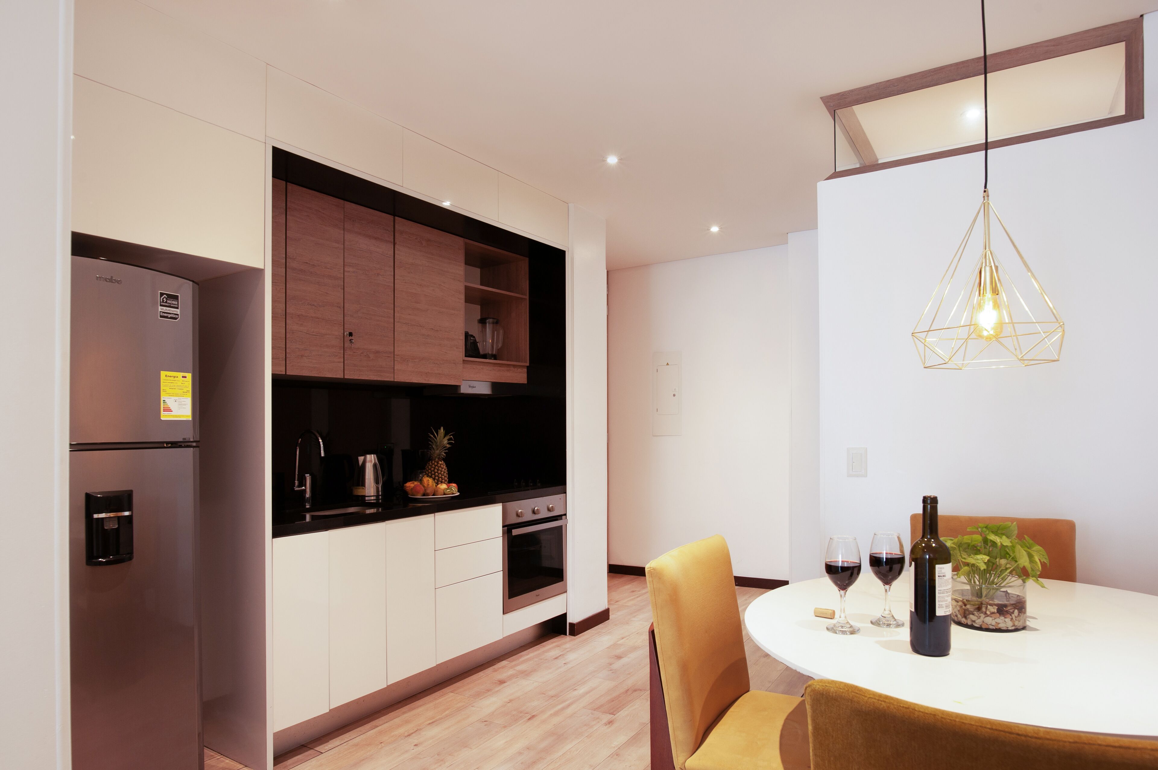 Une cuisine moderne dotée d’appareils électroménagers intégrés, un coin repas avec une table et des chaises, et un luminaire suspendu.
