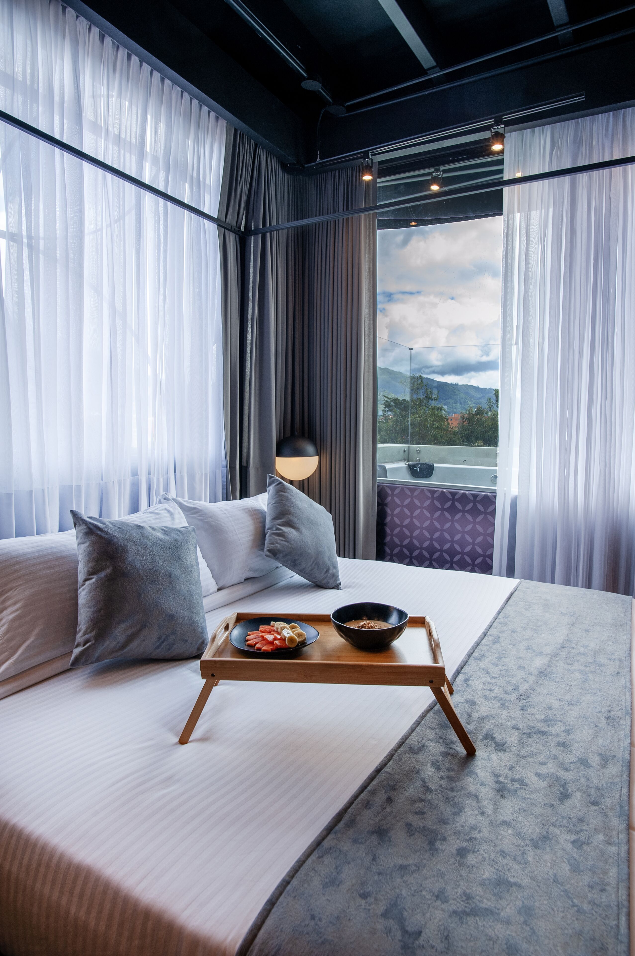 A modern hotel room with a large bed, a tray with snacks, and a view of mountains through the window.