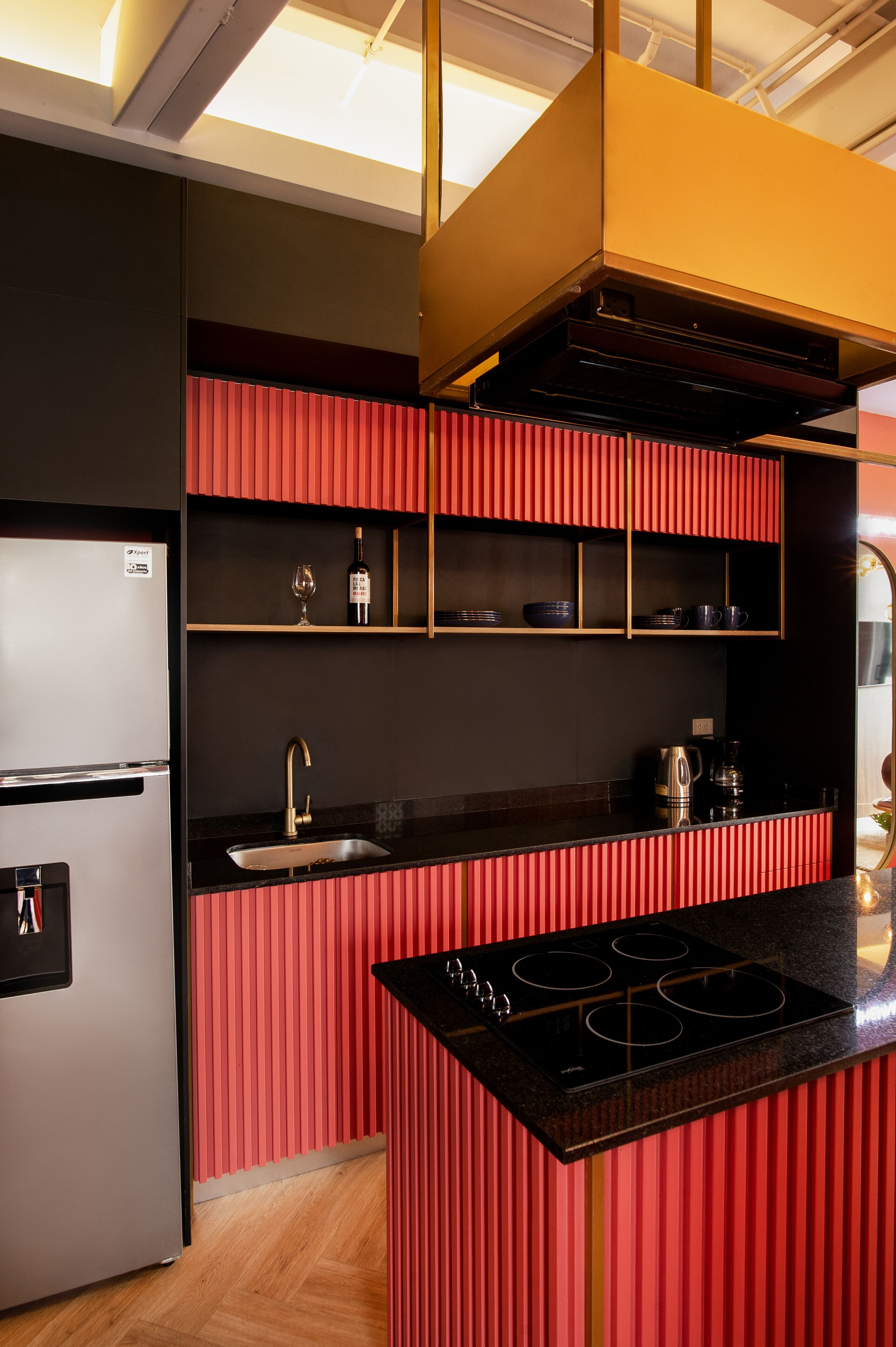 Uma cozinha moderna com geladeira de aço inoxidável, bancada preta, painel de parede vermelho e fogão embutido.