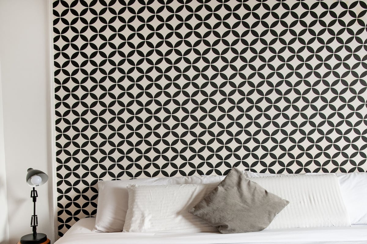 A neatly made bed with a tray of breakfast, including eggs, toast, and coffee, against a geometric patterned wall.