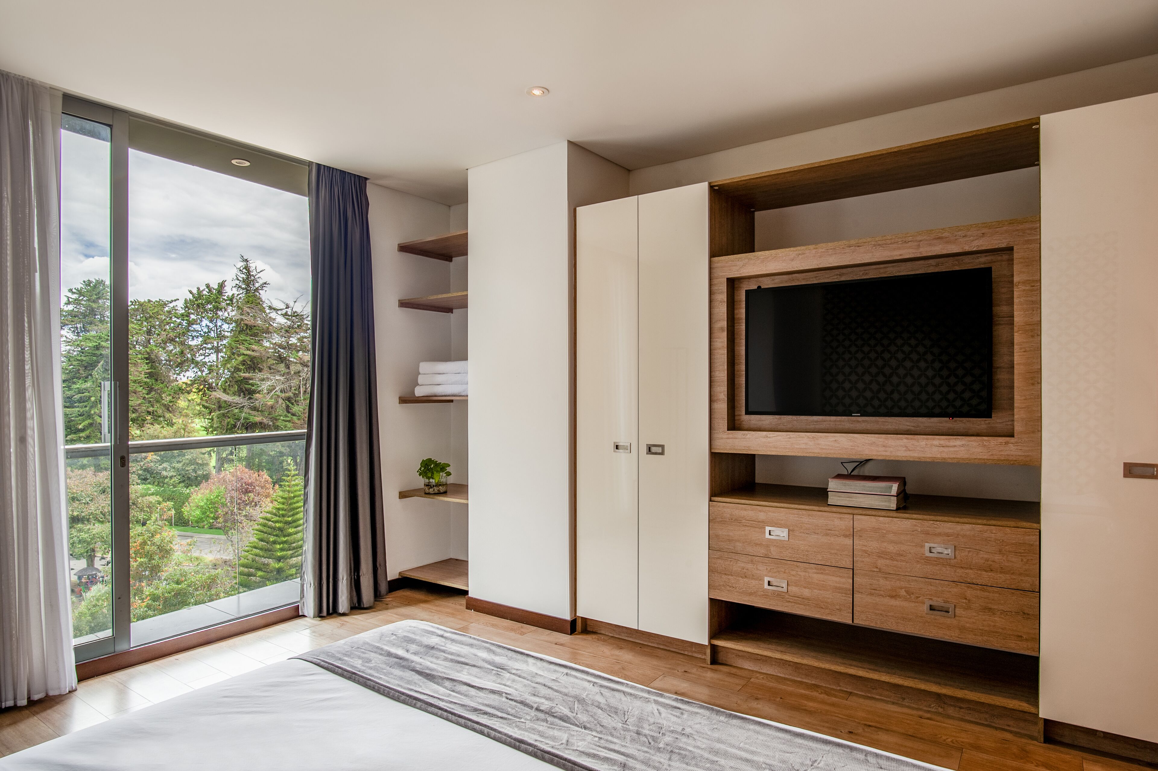 Ein modernes Schlafzimmer mit großem Fenster, integriertem Fernseher und Holzschnitzmöbeln.