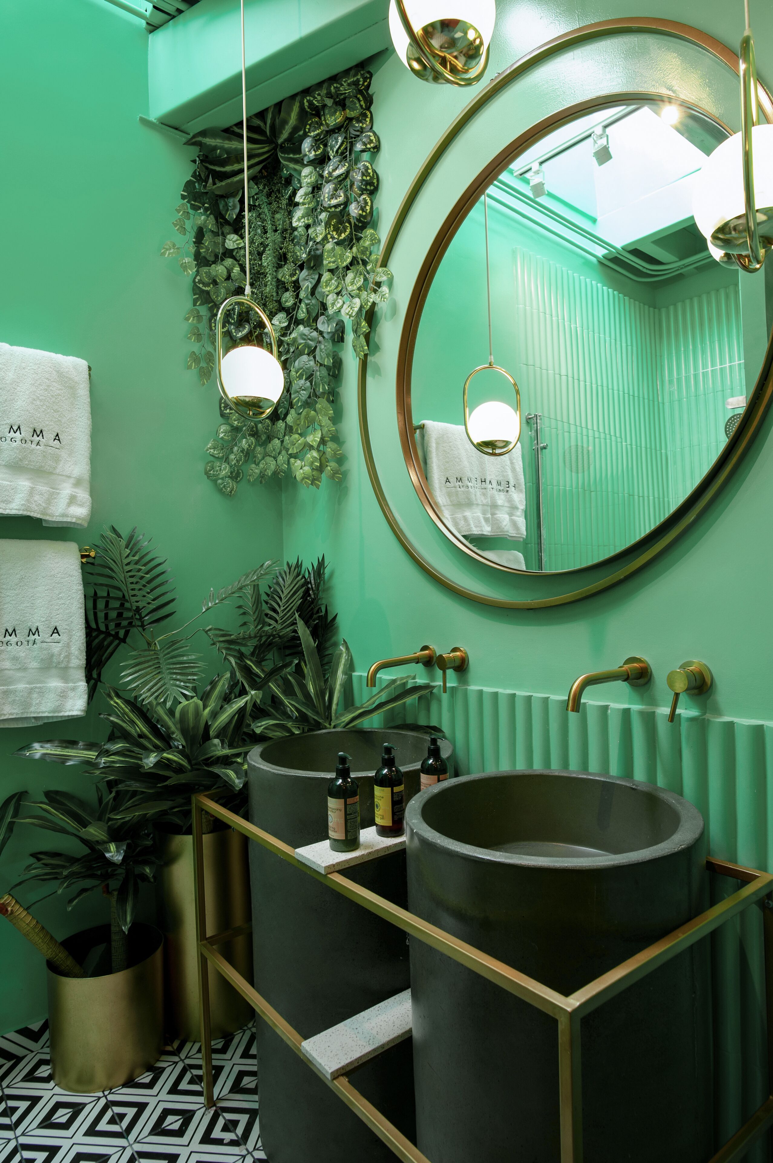 Un baño con pared verde, un espejo redondo, un lavamanos con un recipiente grande y un perchero con toallas.