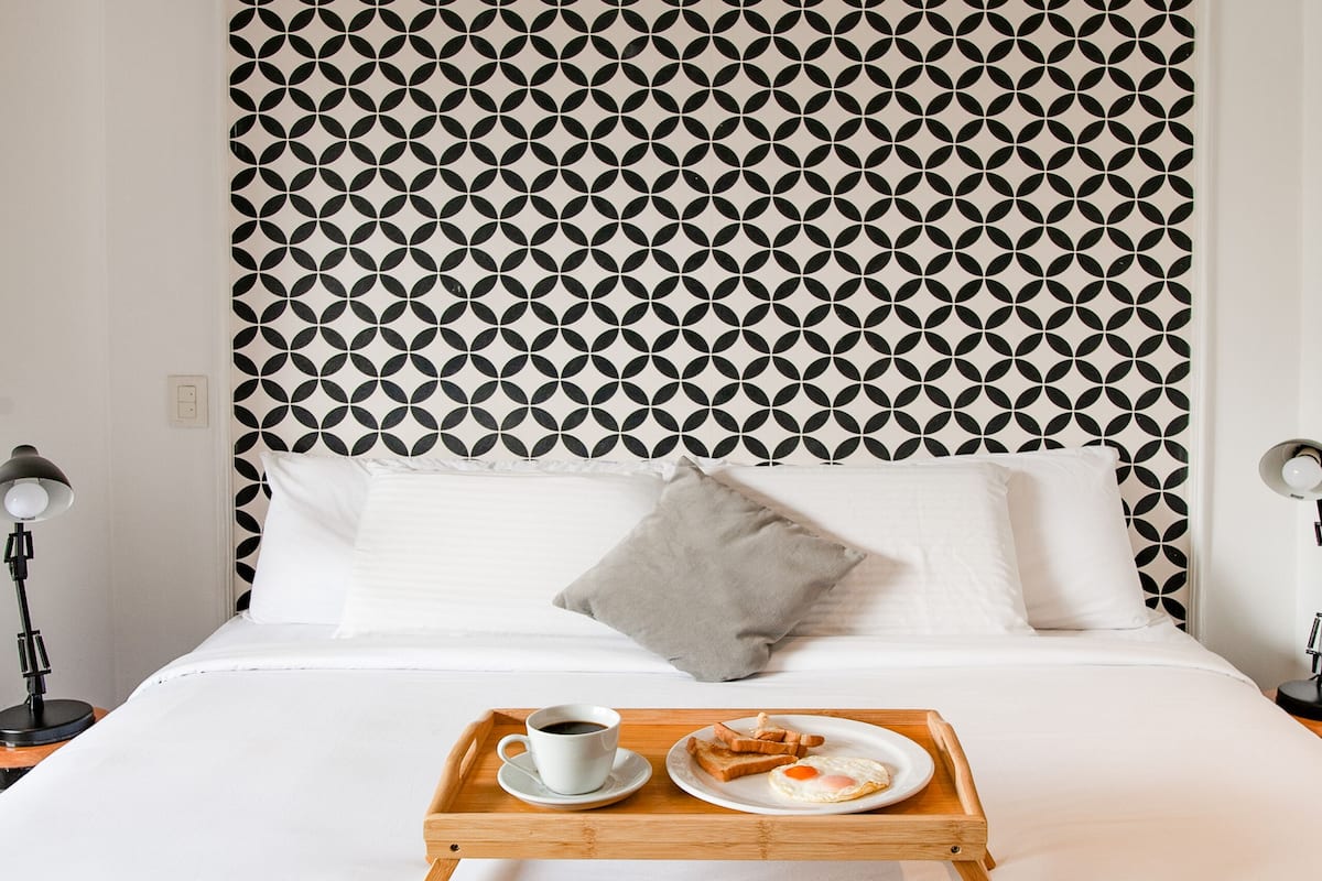 A neatly made bed with a tray of breakfast items, a patterned headboard, and a bedside lamp.
