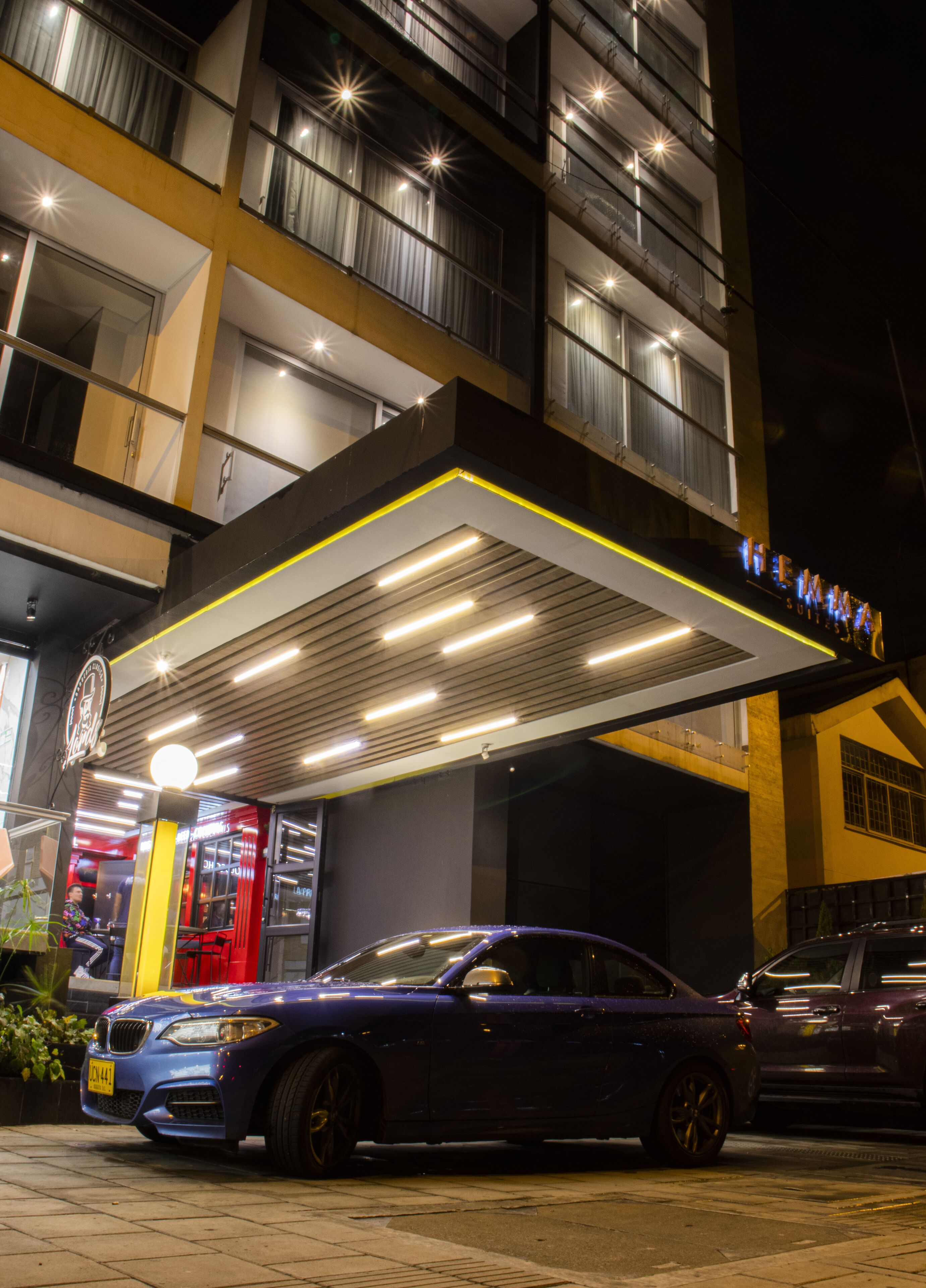 A hotel entrance with a covered parking area, a BMW car parked in front, and a visible sign above the entrance.