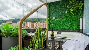 Un balcón con vistas a un paisaje urbano, una pared verde y un jacuzzi.