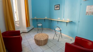 Una habitación con pared azul, una mesa de madera, dos sillas rojas y un reposapiés de madera.