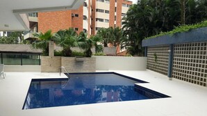 A modern swimming pool with a tiled deck, surrounded by a building with a brick facade and greenery. - BEAUTIFUL APARTMENT IN RIVIERA DE SÃO LOURENÇO, MODULE 4 (Riviera de São Lourenço)
