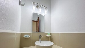 A bathroom with a white sink, a mirror, and three light fixtures above it. - "Experience Tranquility at Hibiscus Studio" (Caye Caulker)