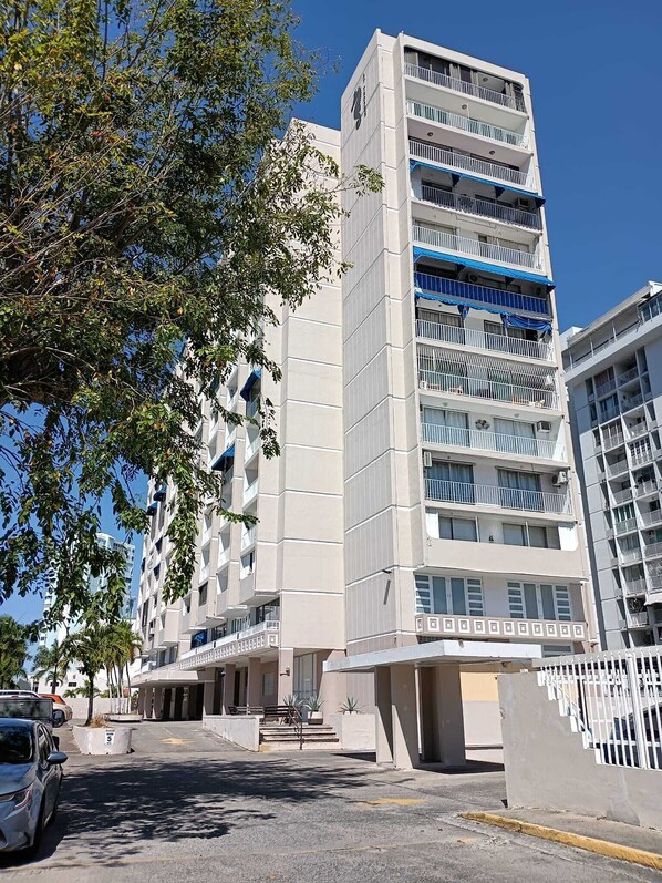 Un edificio de varios pisos con balcones, zona de estacionamiento y cielo despejado.