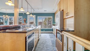A modern kitchen with wooden cabinets, a marble countertop, pendant lights, and a view to the outside. - Luxury Harbor Front Home In Town Chef's Kitchen 4 Ensuite King Rooms + 1/2 bath (Saugatuck)
