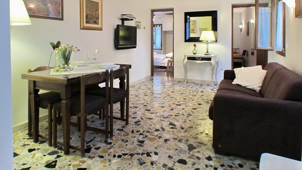 Un área de comedor con una mesa y sillas, un televisor y un sofá en una habitación con piso de baldosas y vigas de techo de madera.