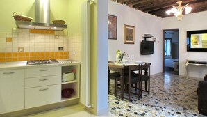 Una cocina con estufa, lavamanos y salpicadero de azulejos. Hay un comedor con una mesa y sillas.