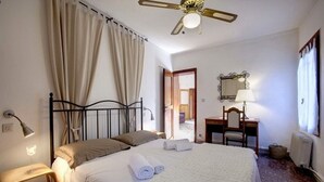 Habitación de hotel con cama, escritorio, silla, lámpara y ventilador de techo.