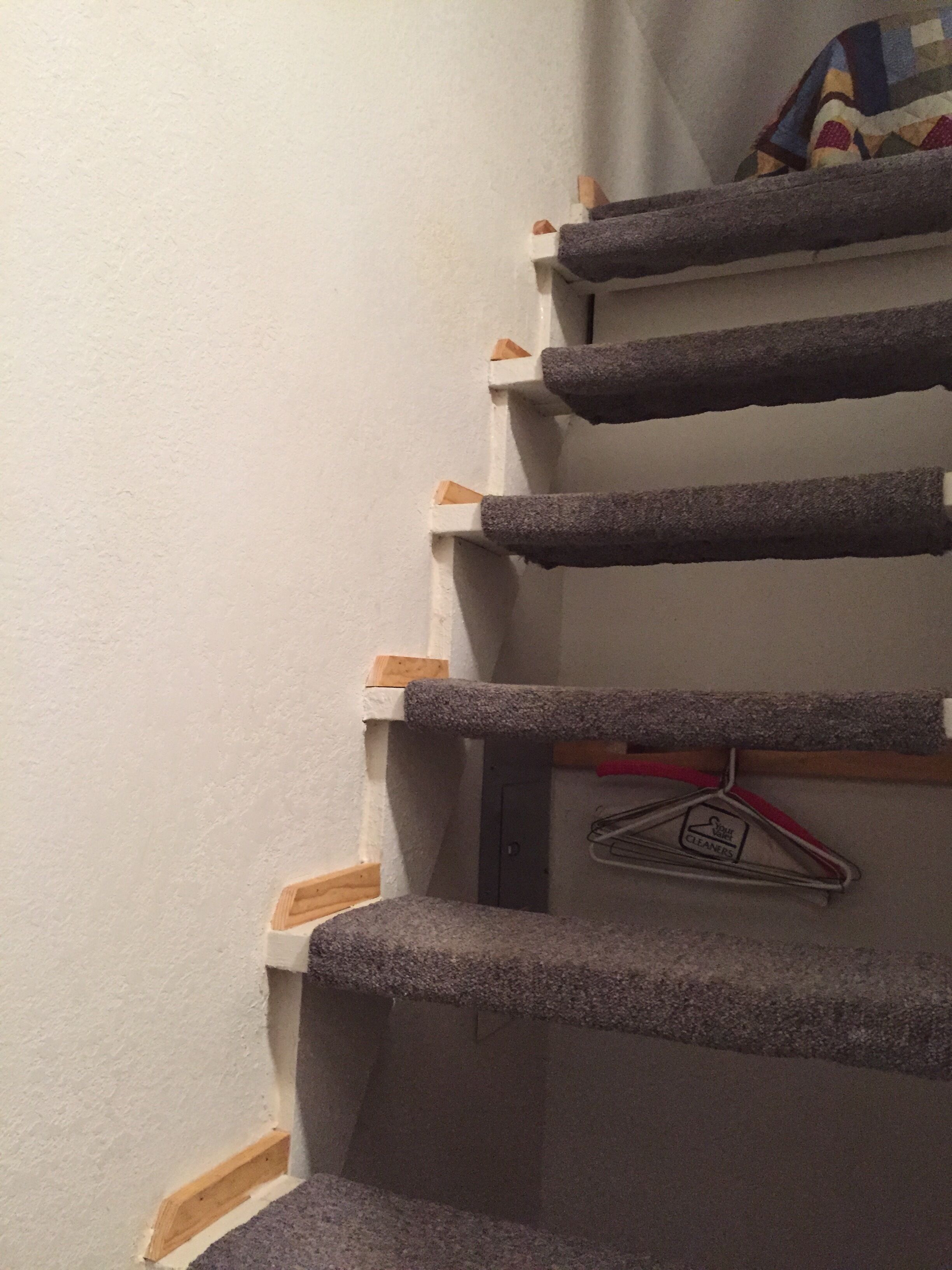 A carpeted staircase with wooden handrails and a metal hanger with a cleaning symbol.