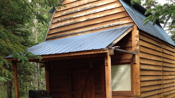 Eine Holzhütte mit Veranda, Grill und einer kleinen Sitzecke.