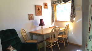 Ein Essbereich mit einem Holztisch, vier Stühlen, einer Lampe und gerahmten Kunstwerken an der Wand.
