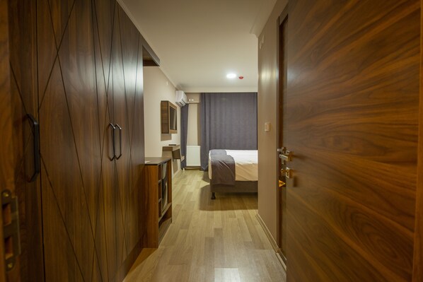 Habitación de hotel con un armario de madera, una cama con edredón gris, una mesita de noche y un espejo.
