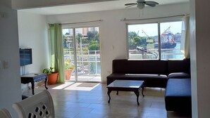 Un vaste espace de vie avec un balcon, un canapé, une table basse et une table à manger agrémentée de fruits.