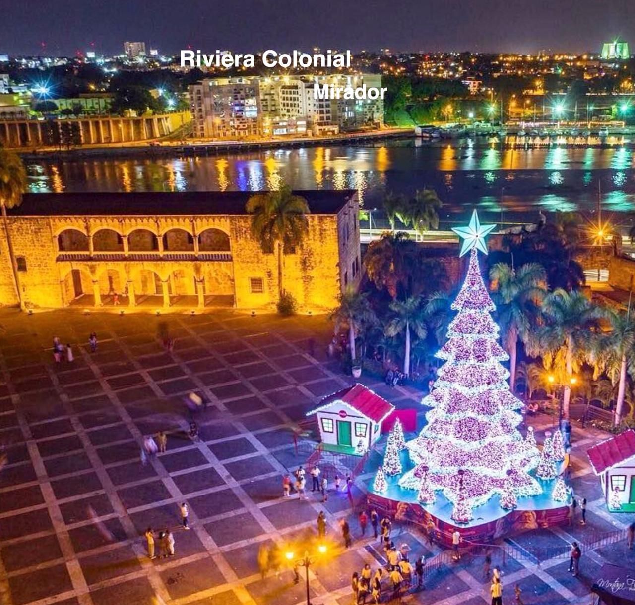 Una plaza con un gran árbol de Navidad y una estrella en la cima, rodeada de gente y edificios.