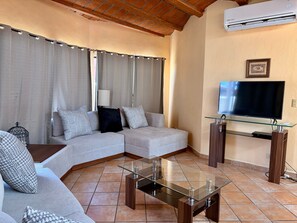 Ein Wohnzimmer mit einem Ecksofa, einem Glastisch, einem Flachbildfernseher auf einem Holzboden und einem Deckenventilator.