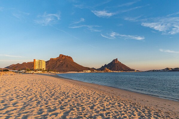 Ein Strand mit einem Hotel und Bergen im Hintergrund.